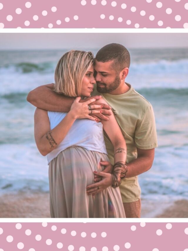 Expecting parents embracing on a beach during a babymoon getaway.