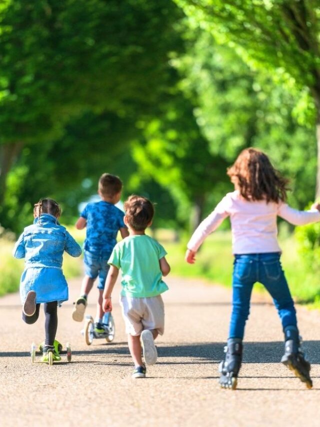 Children riding scooters together on a paved park path.