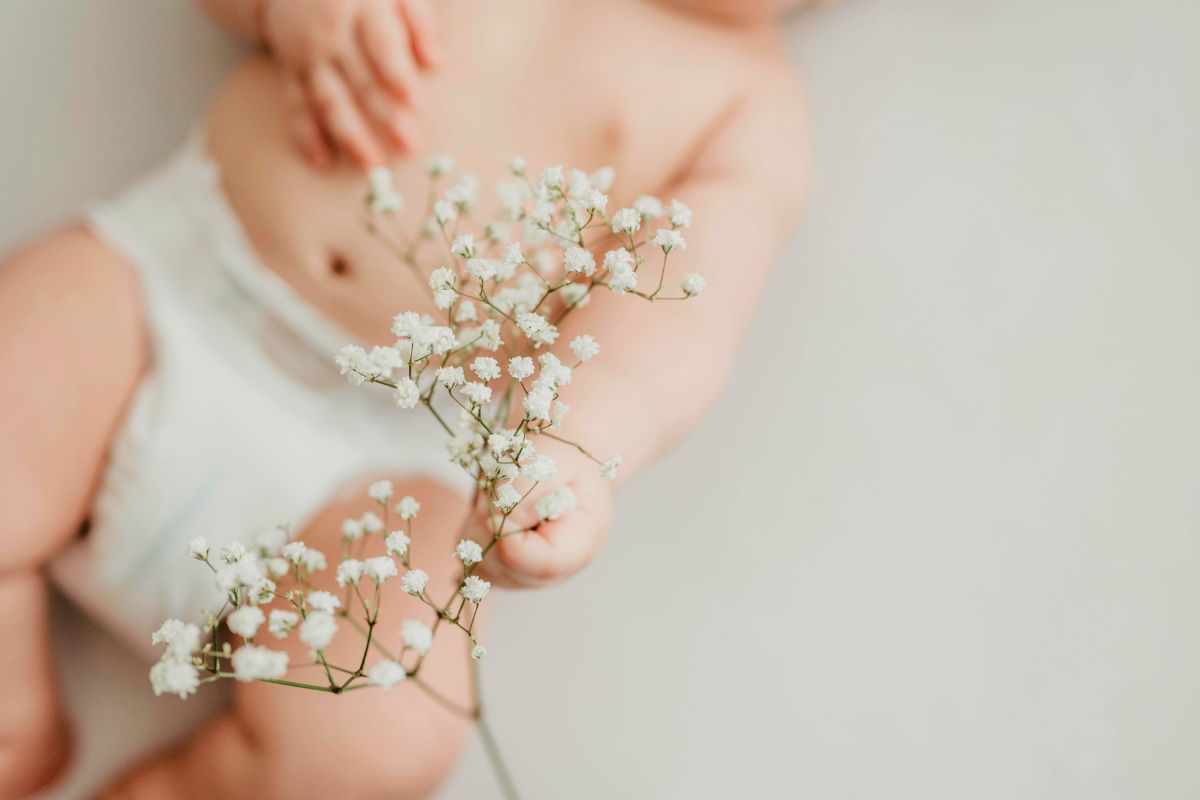 Baby in a diaper holding flowers during the infant stage when diaper blowouts and diaper leaks are common.
