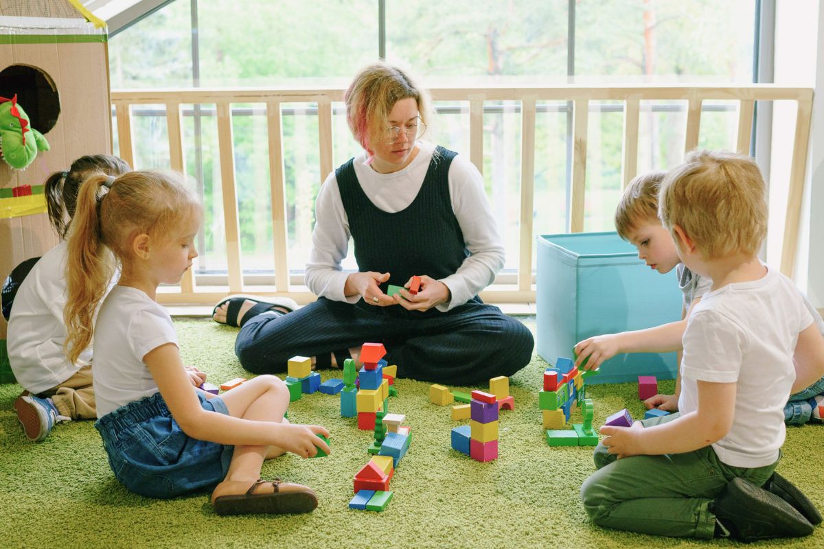 Teacher and young children playing with blocks during daycare or preschool group activity.
