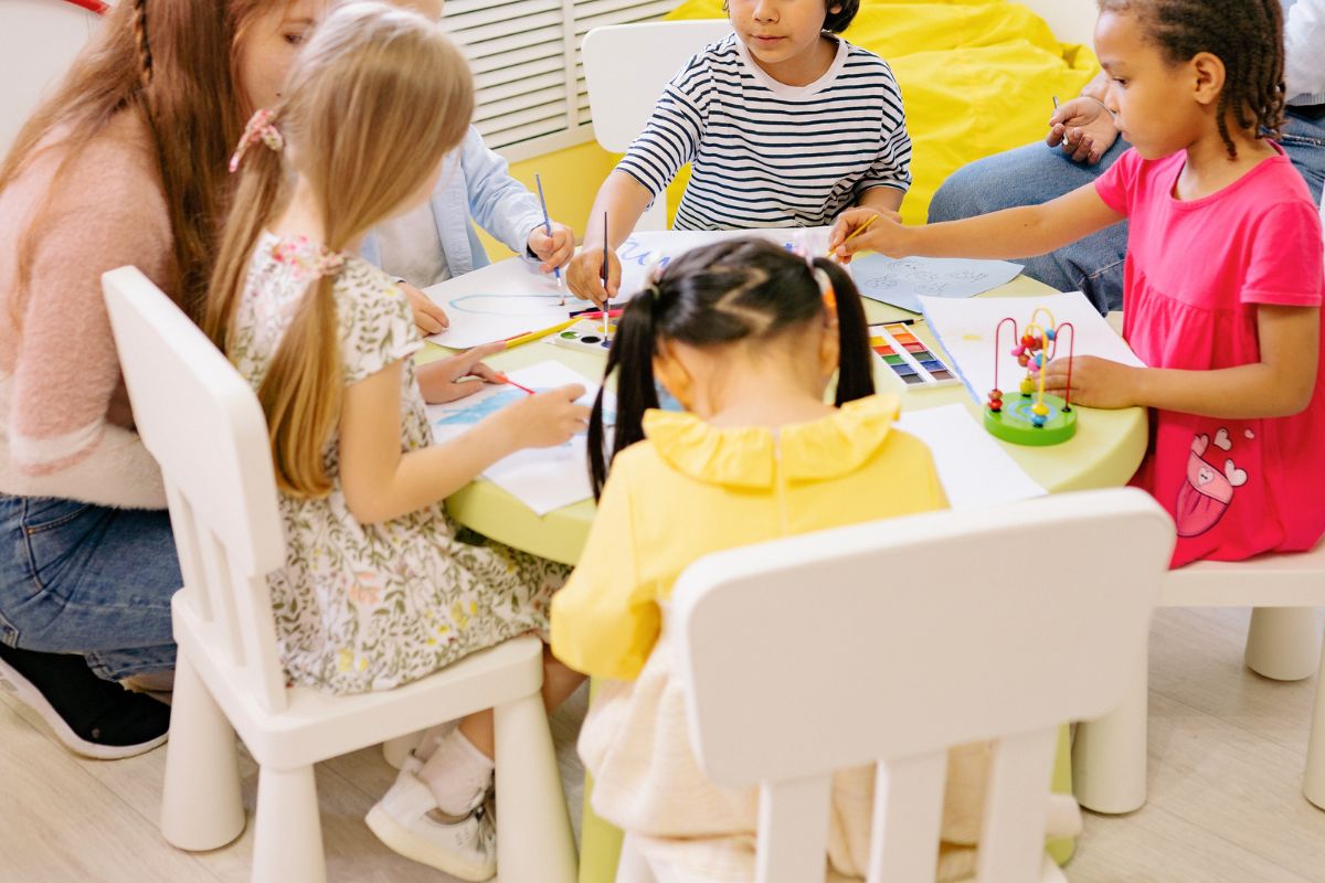 Young children drawing and painting together at a preschool classroom table.