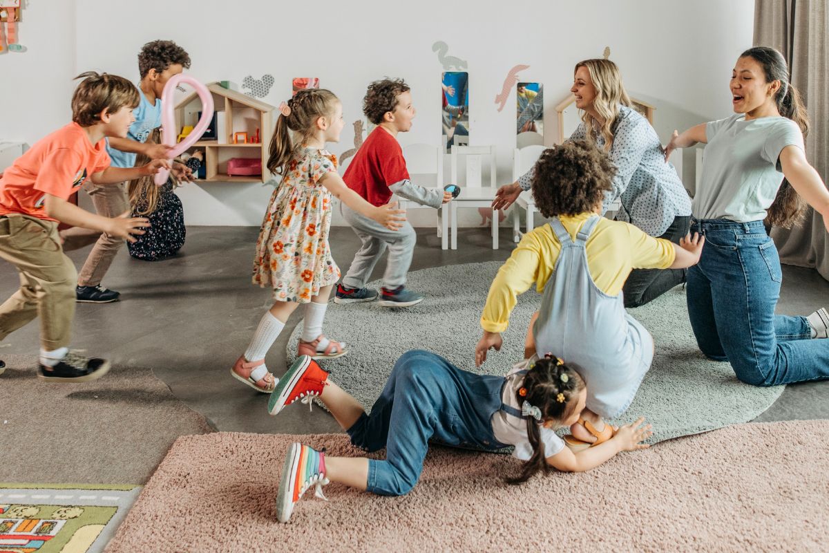 Daycare children playing an active group game with teachers in the classroom.