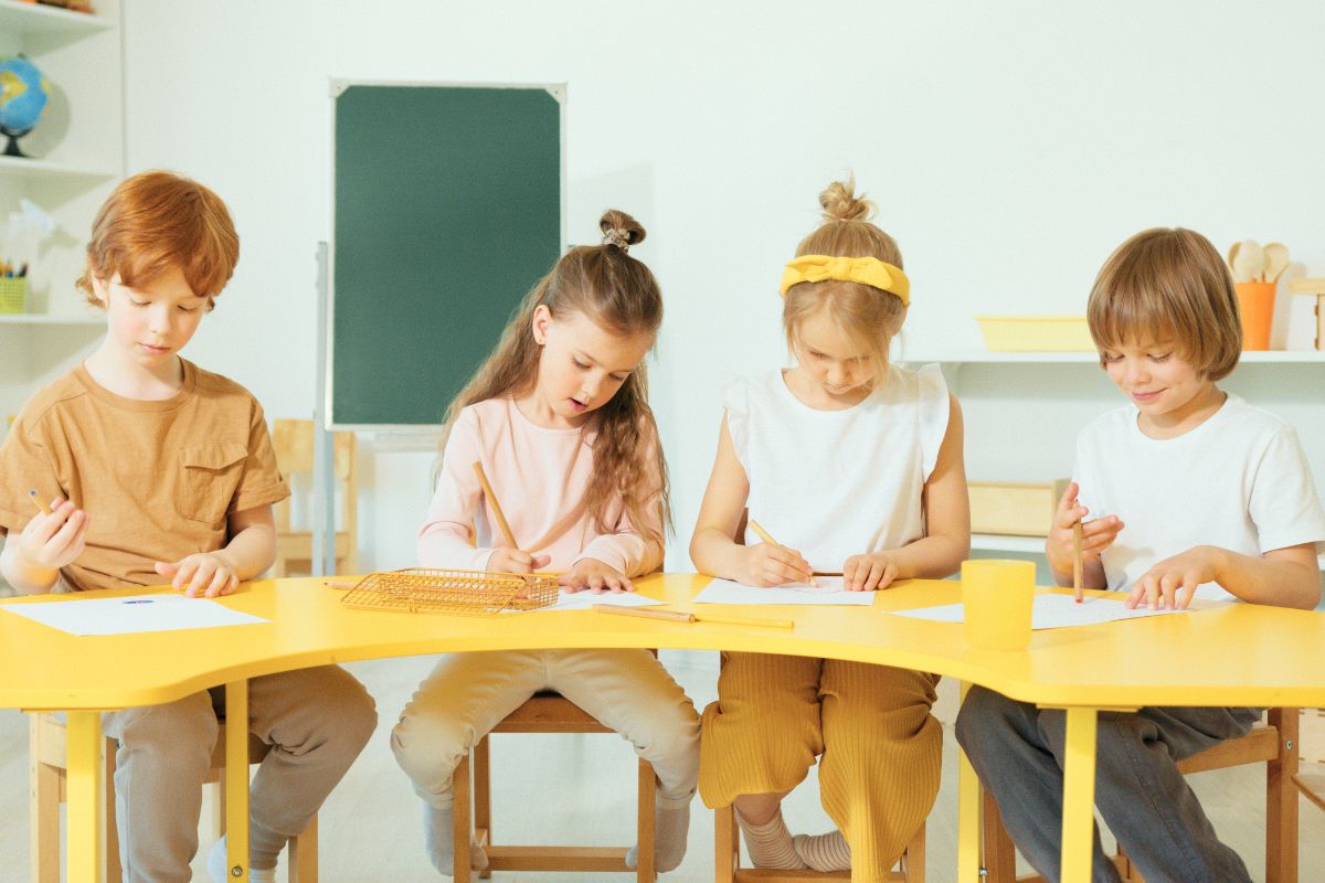 Kindergarten-age children practicing writing and drawing at a classroom table.