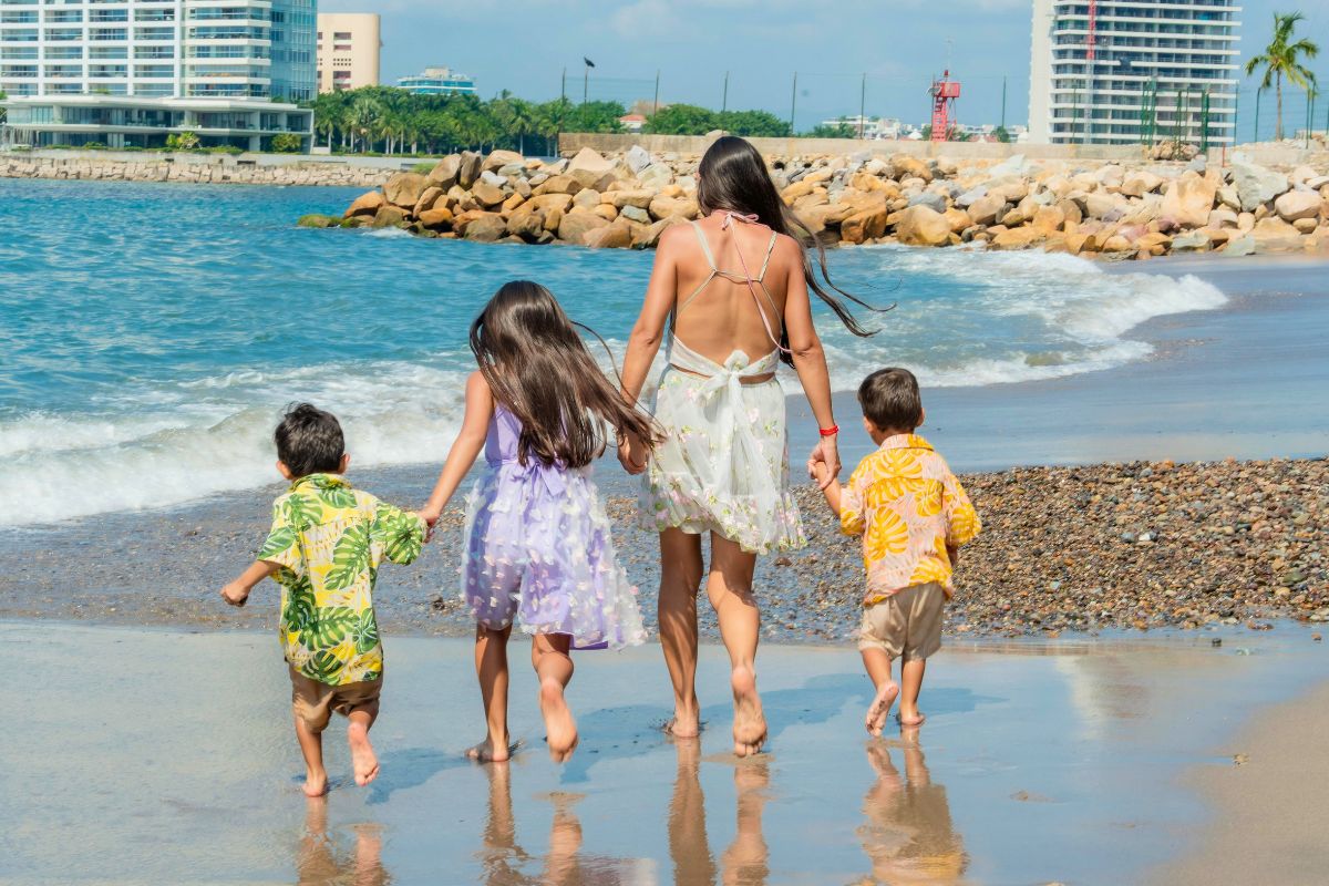 Mother walking along the beach with three young children during a family beach vacation.