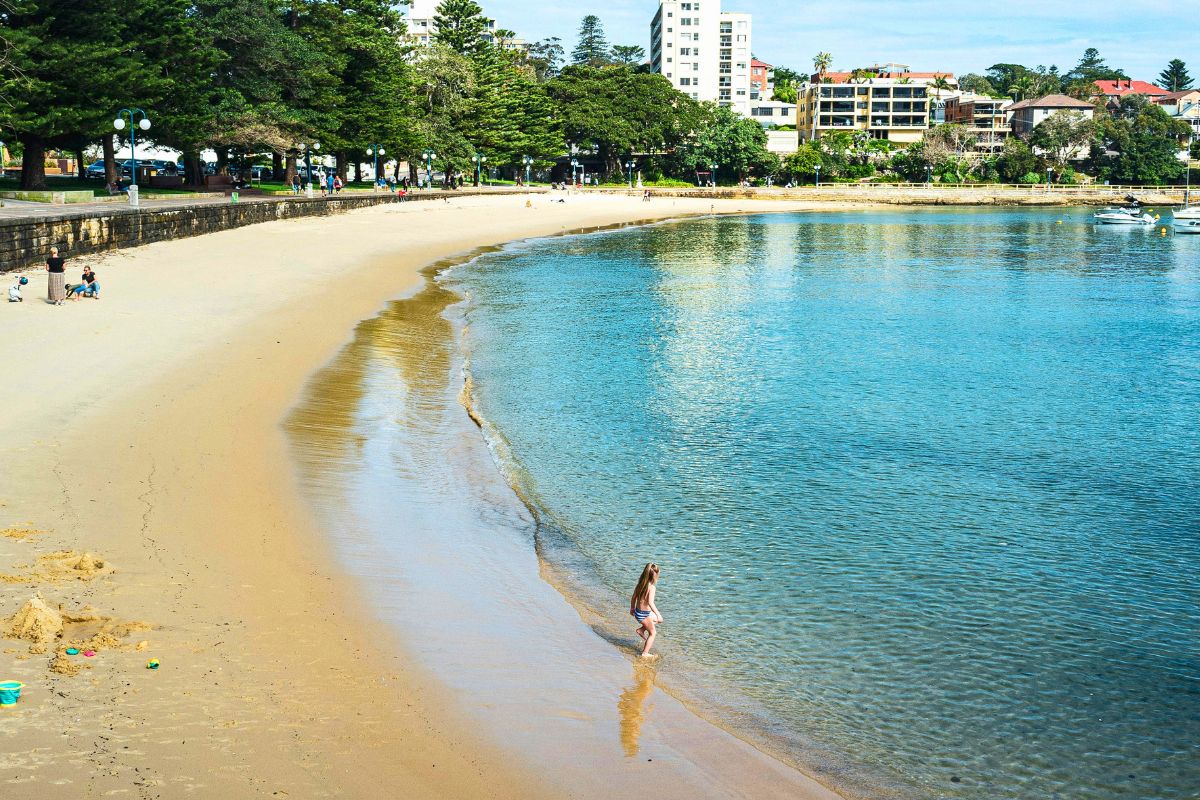 Young child standing on a calm sandy beach with shallow water, perfect for family-friendly beach vacations.