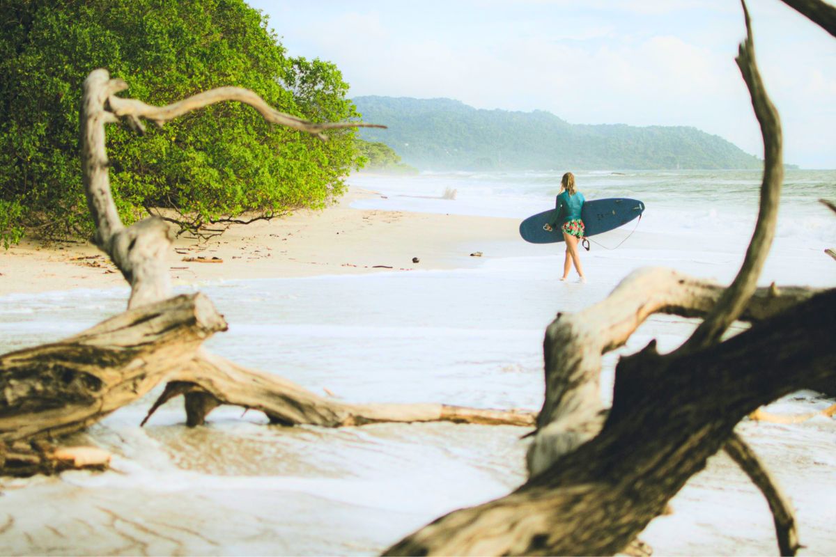 Surfer walking along Tamarindo Beach in Costa Rica, a family-friendly destination known for surfing and outdoor adventures.