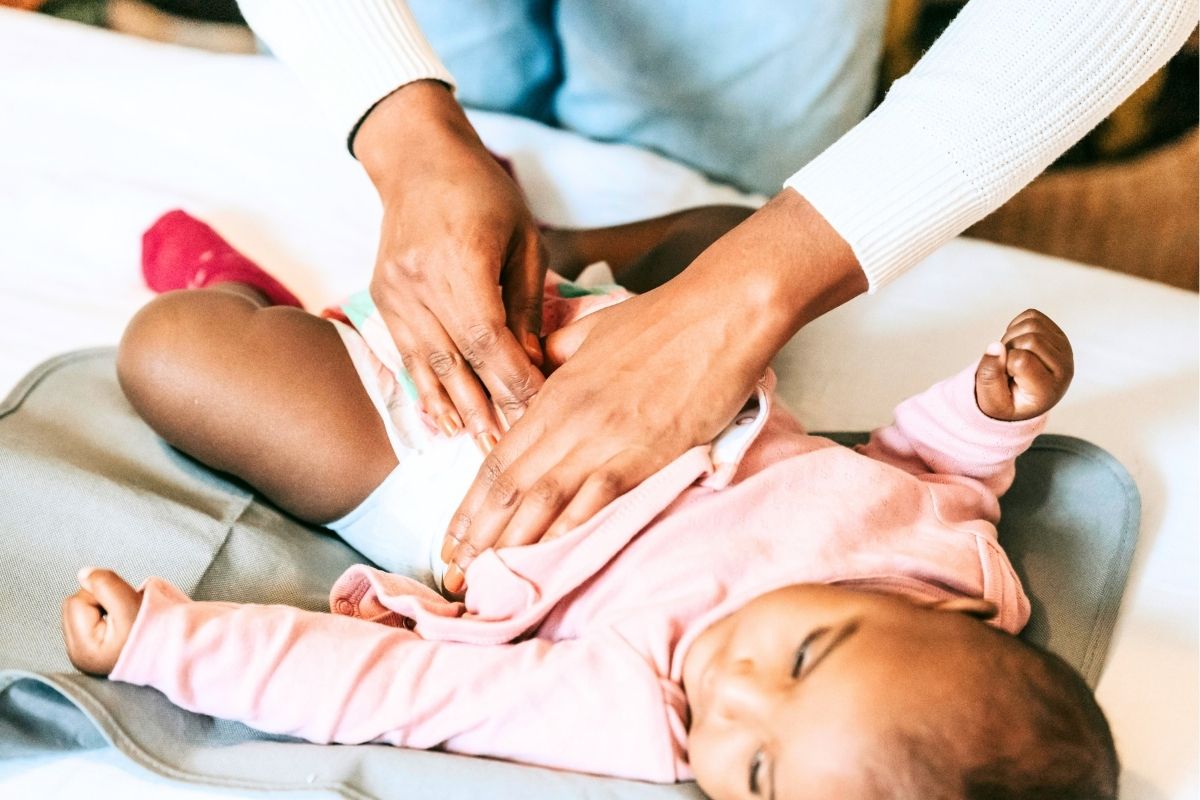 Mother fastening a diaper on a baby lying on a soft pink blanket.