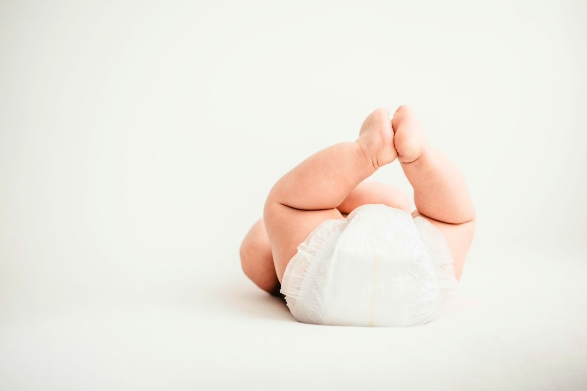 Baby lying on their back with legs raised while wearing a diaper against a neutral background.