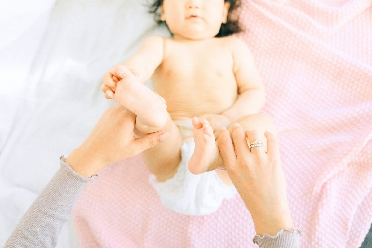 Baby lying on her back with parent's hands holding her feet.