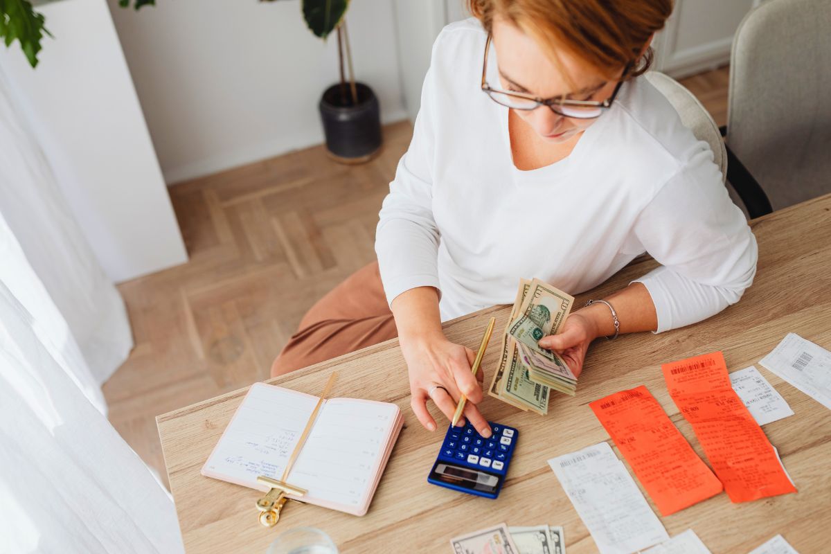 Parent calculating expenses with calculator, cash, and receipts while budgeting for a large family.