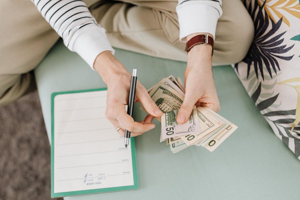 Person writing in a budget planner while holding cash to manage a large family budget.
