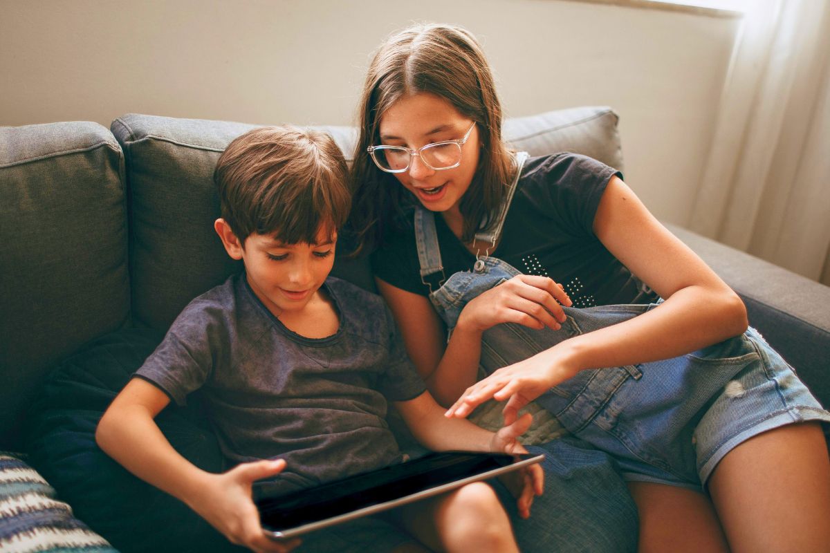 Two children sitting on a couch and watching YouTube Kids on a tablet.