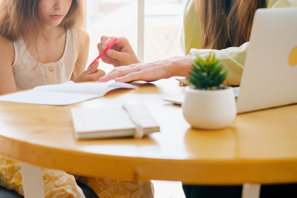 Parent helping a child complete homework at the table while using ChatGPT to explain schoolwork.