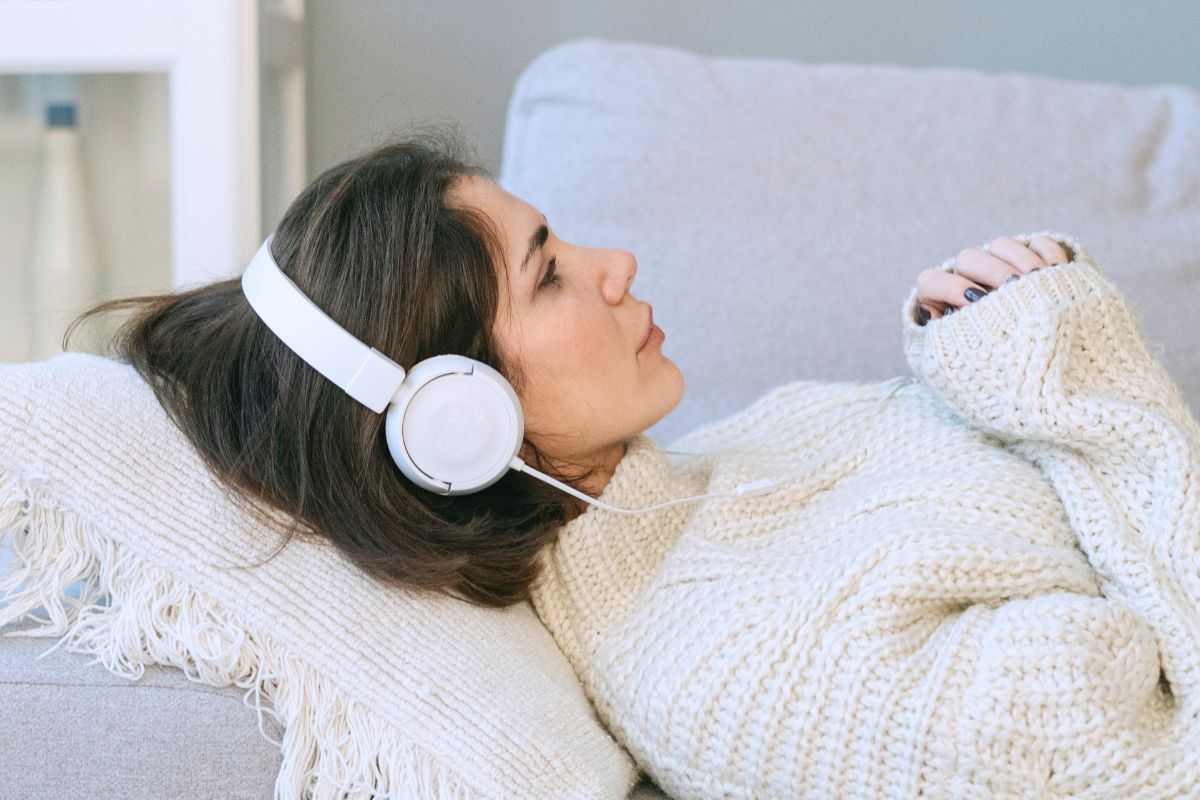 Pregnant woman resting with headphones as part of a calming pregnancy self-care routine.