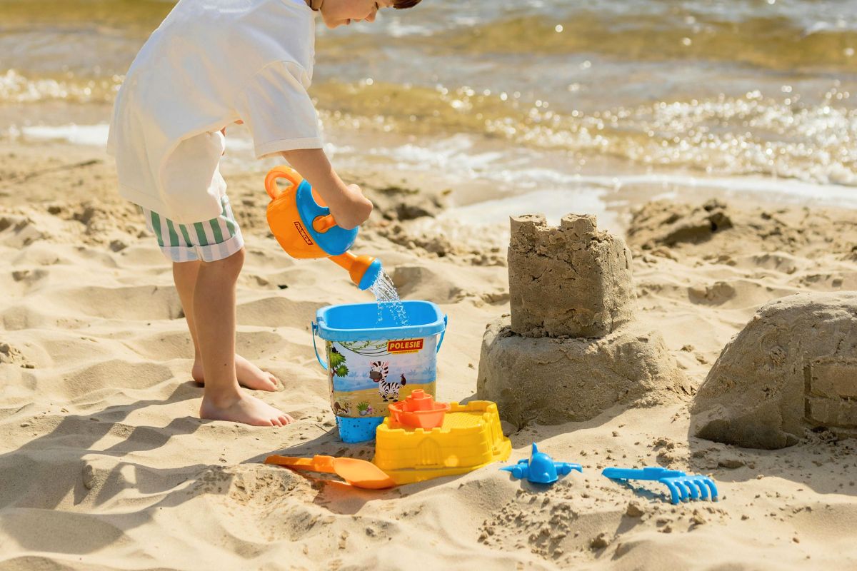 Toddler playing with sand toys by the beach with bucket and shovel for toddler beach packing list.