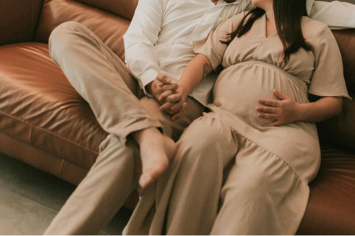 Expecting couple holding hands on the couch, enjoying a quiet and romantic pregnancy date night at home.