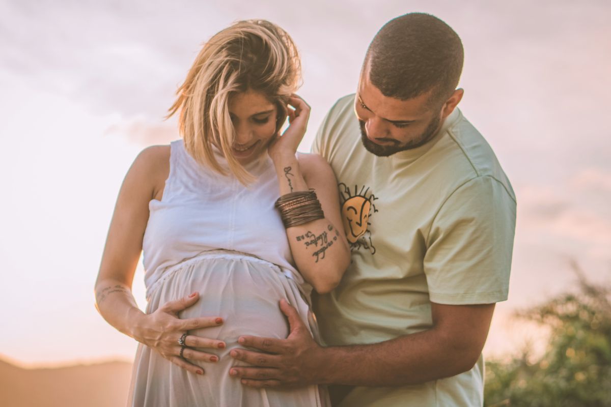 Pregnant couple smiling outdoors while holding the baby bump, creating sweet memories before baby arrives.