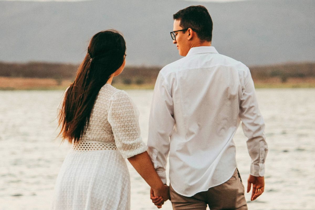 Pregnant couple walking hand in hand by the water, enjoying a calm and low stress date before baby comes.