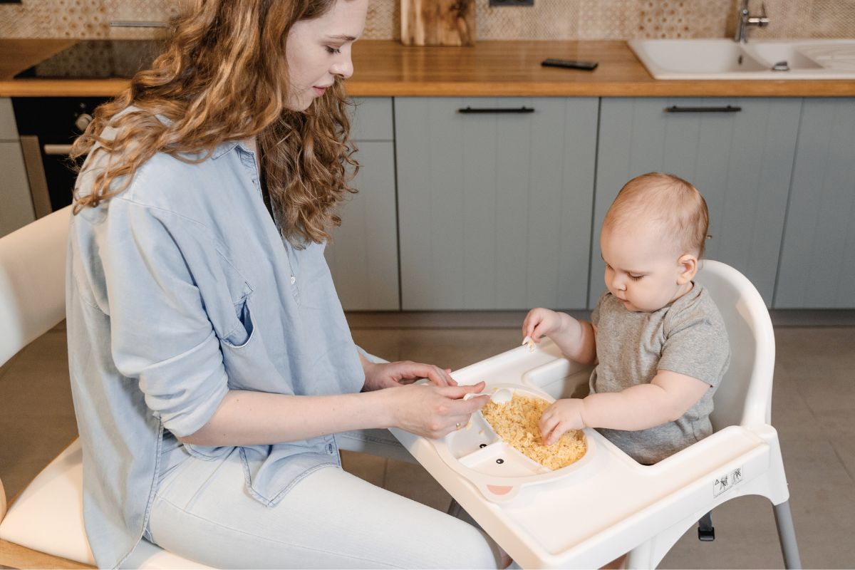 Mother feeding her baby in a high chair while preparing for a busy daily routine.