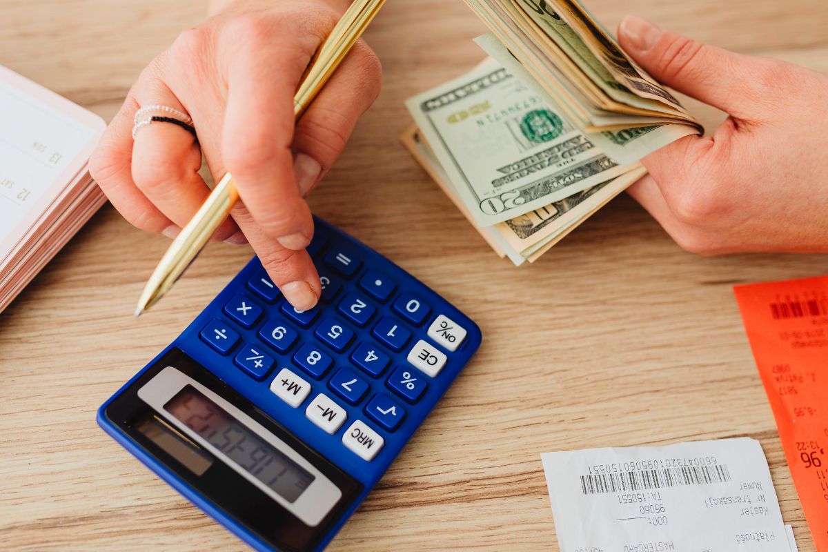Person calculating grocery expenses with cash and calculator at home.