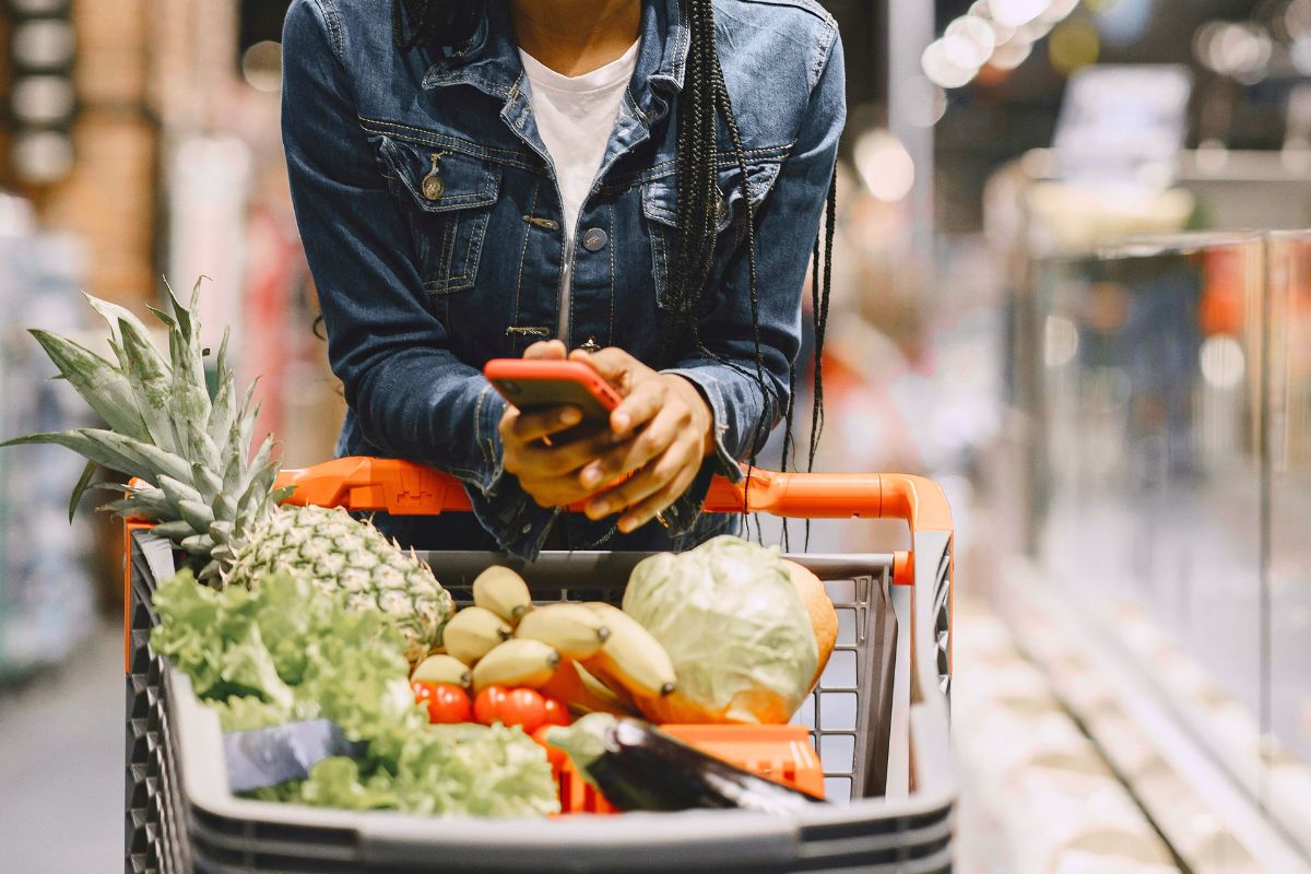 Woman using phone while grocery shopping for affordable family meals.