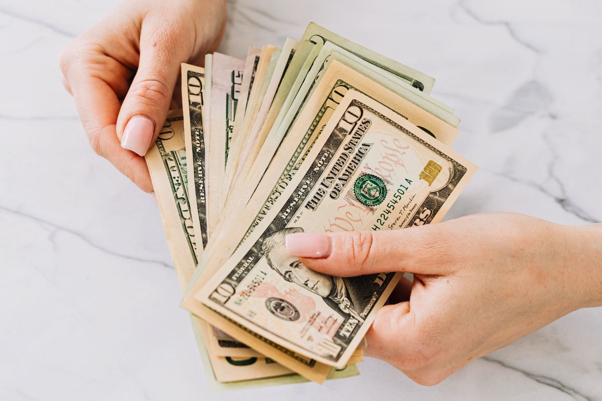 Hands holding cash for simple grocery budgeting and saving money tips.