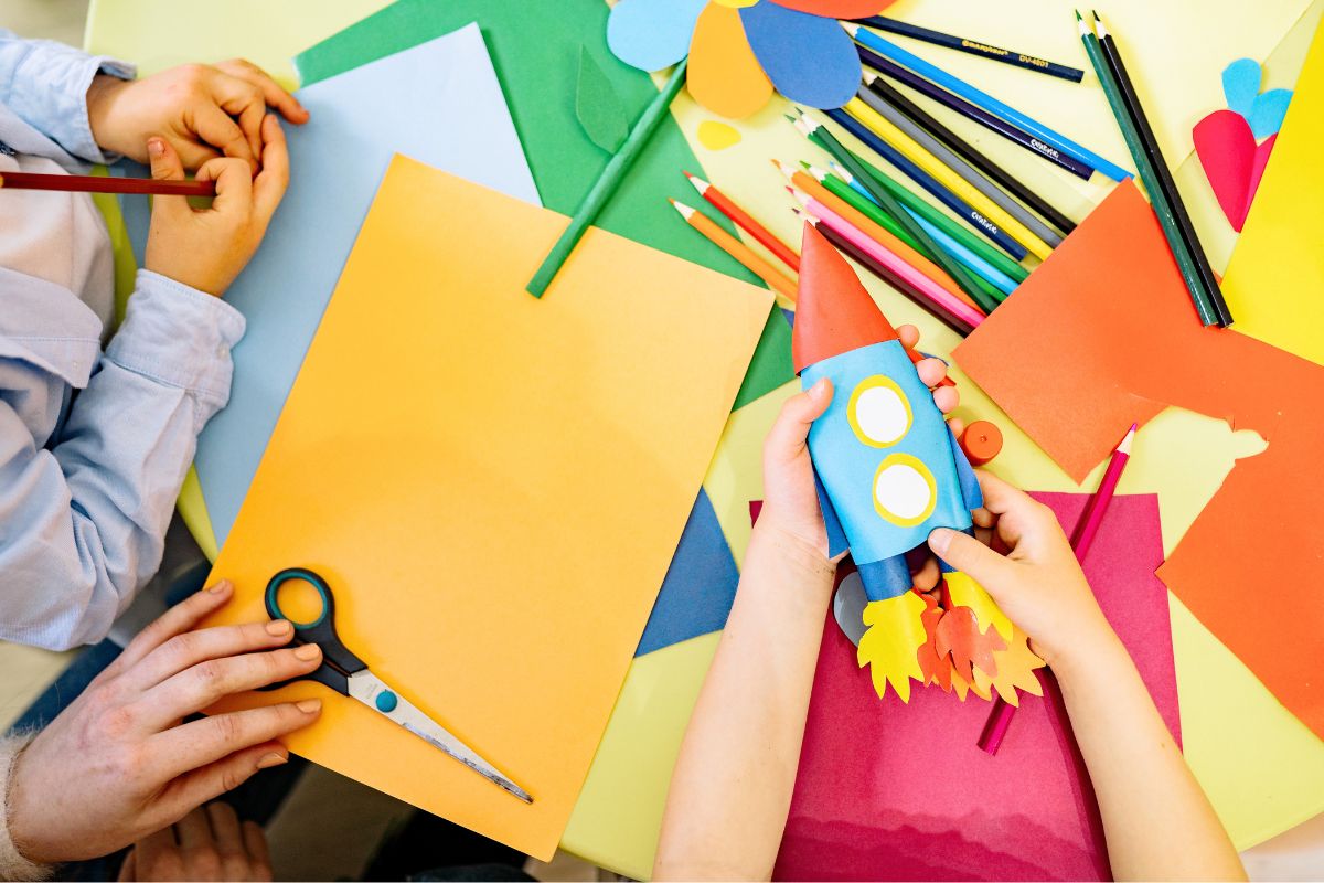 Children using pencils, scissors, and colored paper from their back-to-school supply list for a classroom craft.