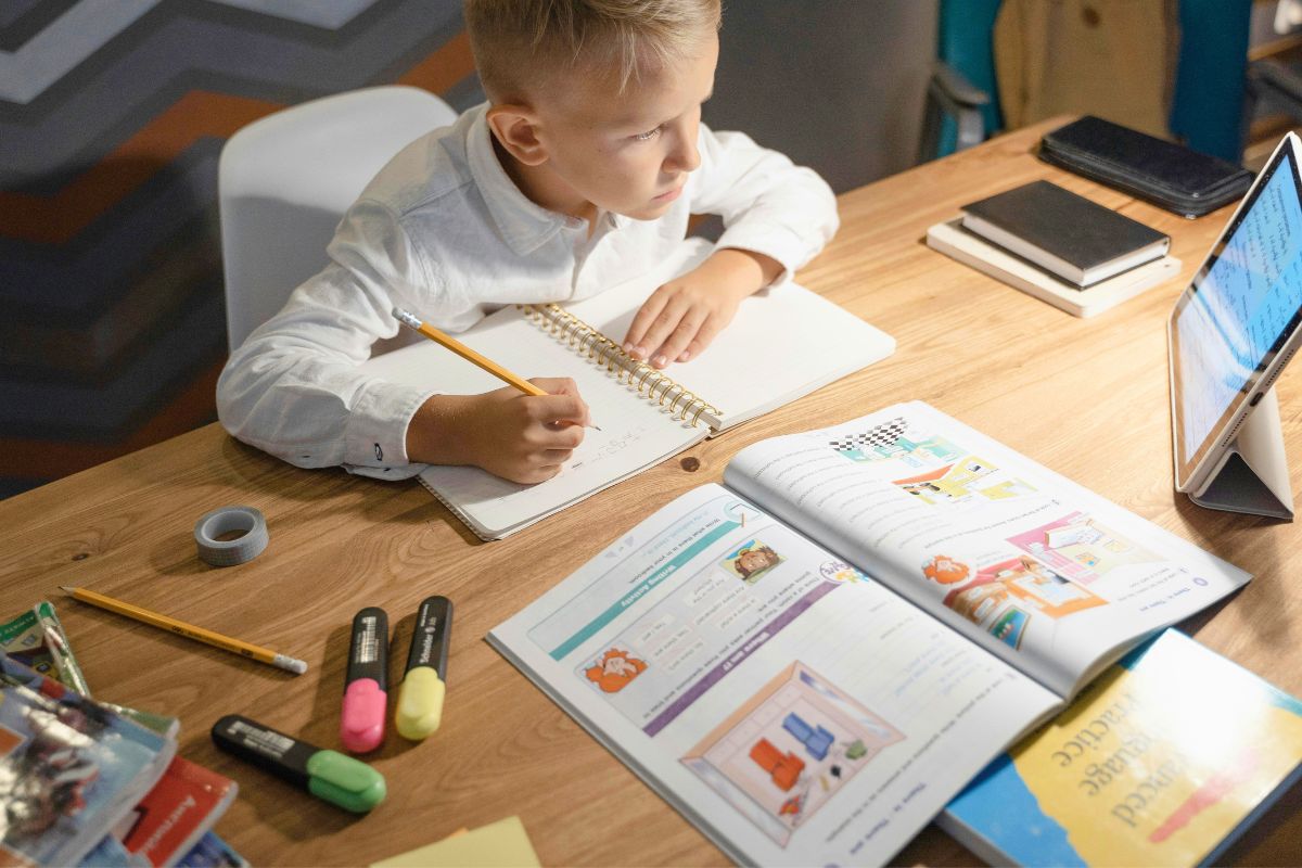 Child completing homework at an organized desk with notebooks, pencils, highlighters, and a school-approved tablet.