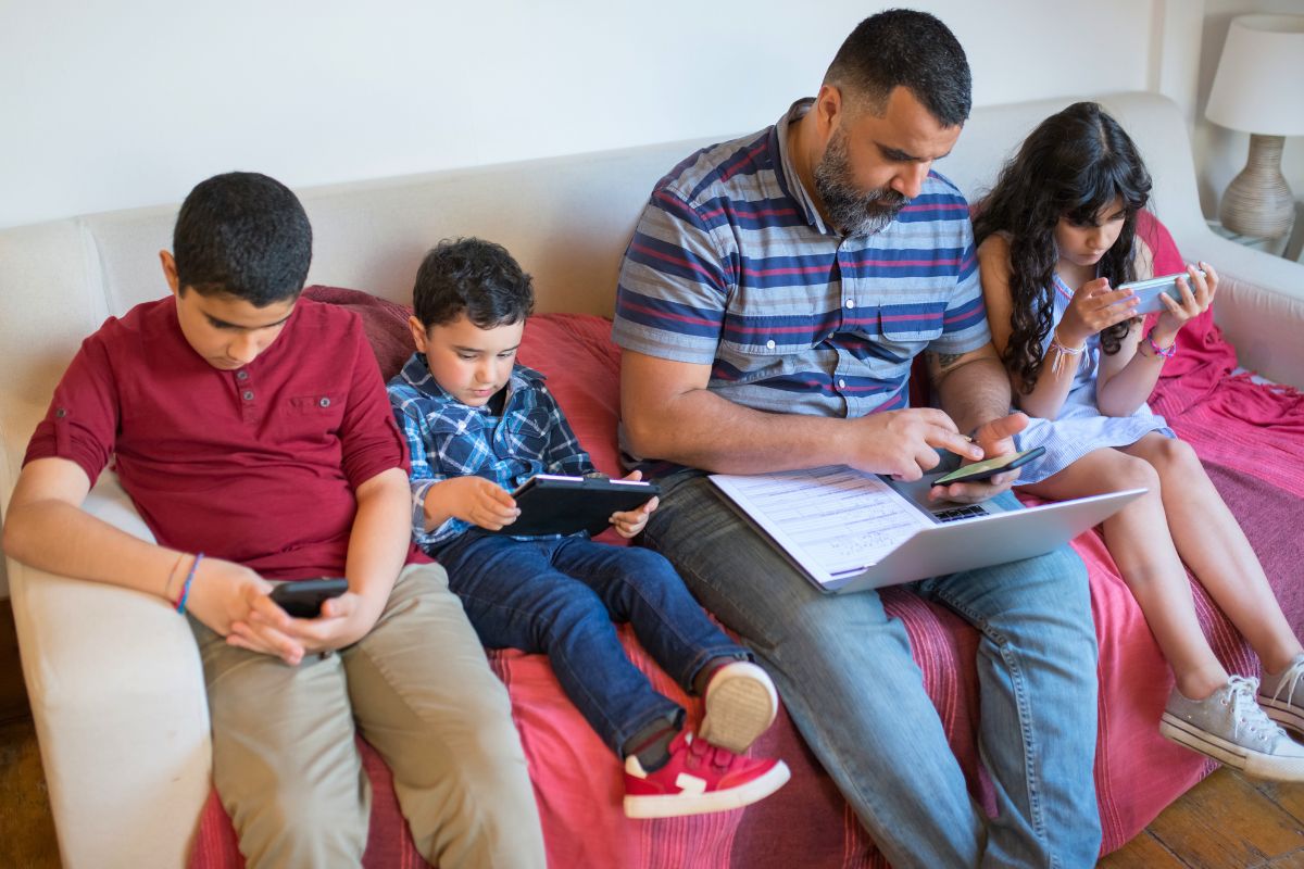 Father supervising his children as they use digital devices and learn responsible technology habits.