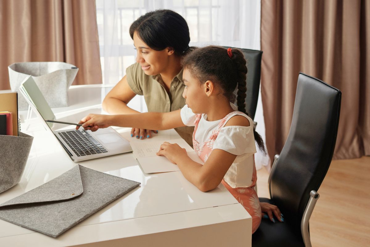 Mother helping her daughter learn on a laptop during a supervised technology activity at home.