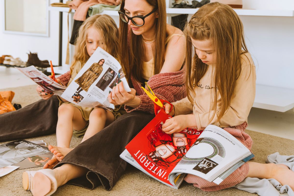 Mother and two daughters creating a craft project with magazines, paper, and scissors.