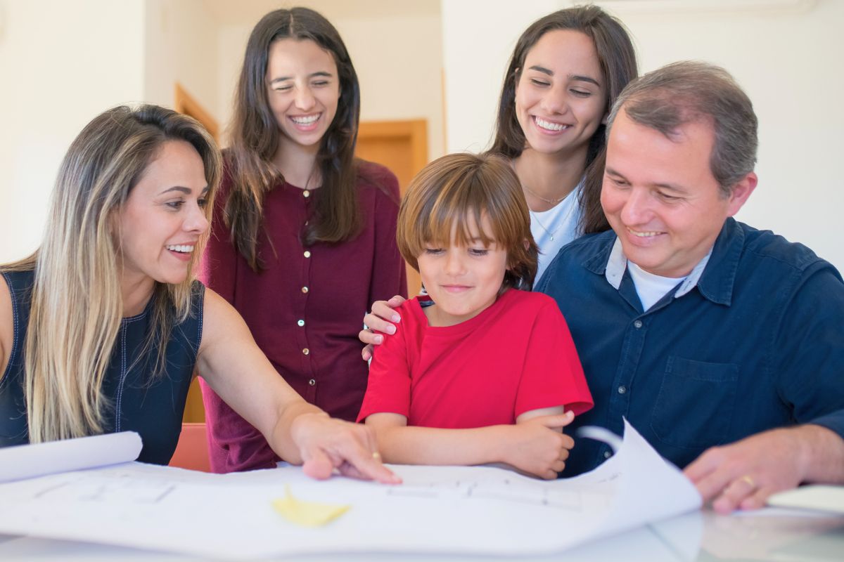 Parents and older children helping a young boy with a family learning activity at the table.