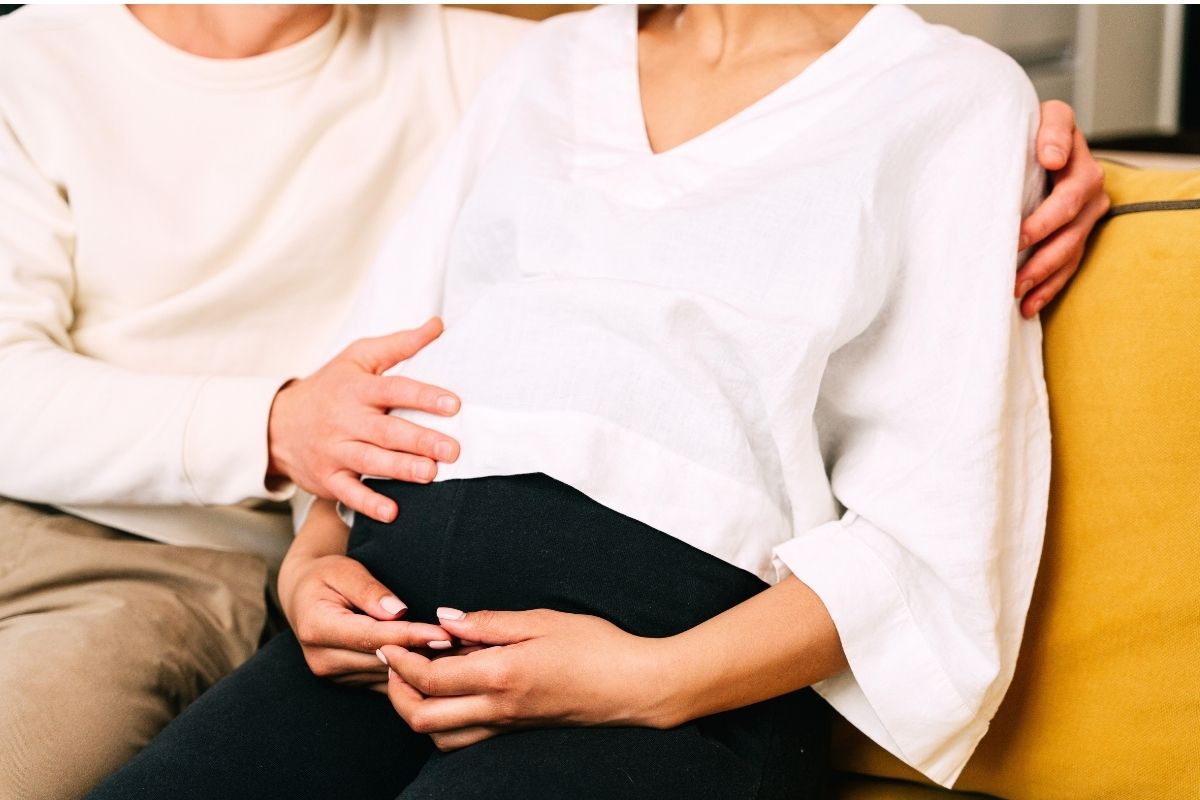 Close-up of pregnant woman holding her belly while wearing a white shirt.
