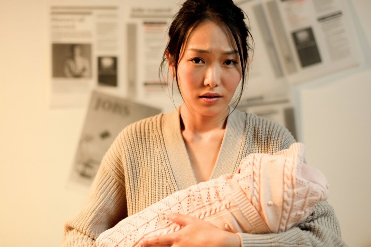 Anxious mother holding her newborn baby, sitting indoors.