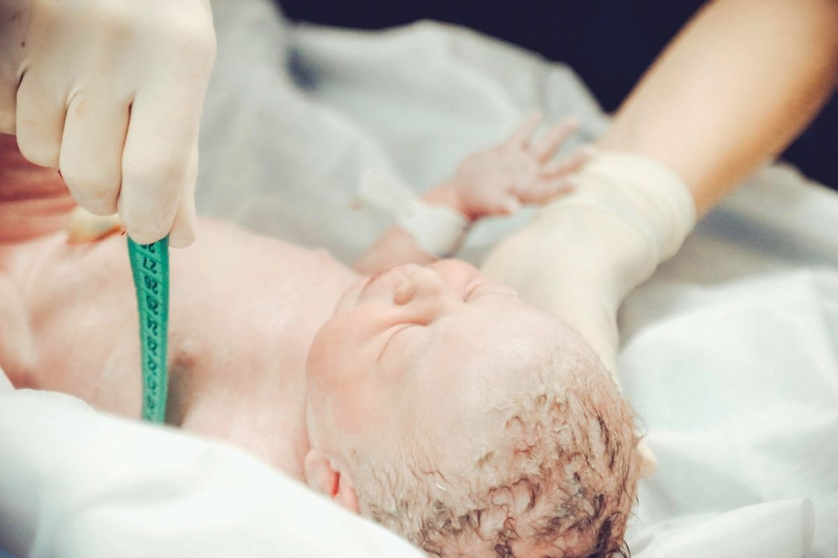Close-up of a newborn baby lying on a hospital bed, swaddled in a blanket.