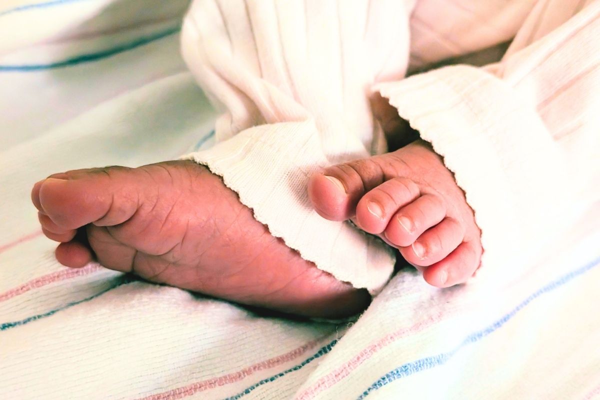 A babies feet on striped bed sheets and wearing long pants.