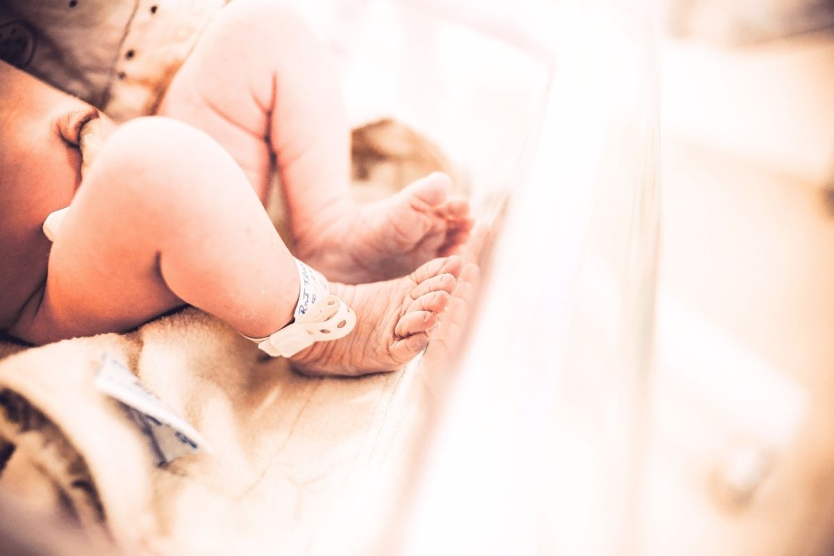 Newborn baby on a bed, wearing a hospital tag.