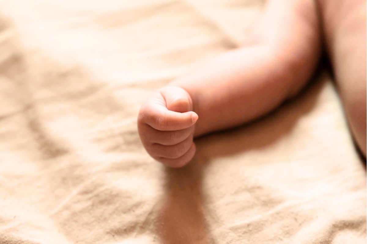 Babies arm and hand on a white linen sheet.