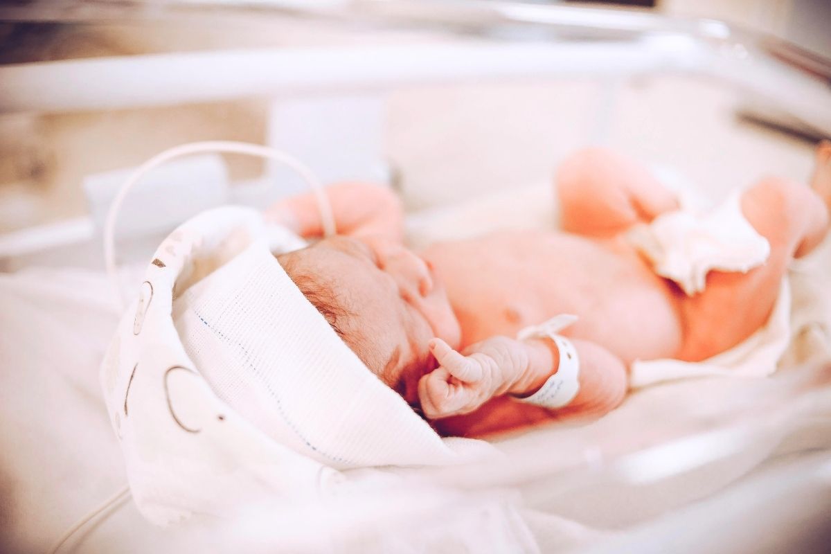 Newborn in a hospital bassinet with white bed linen.