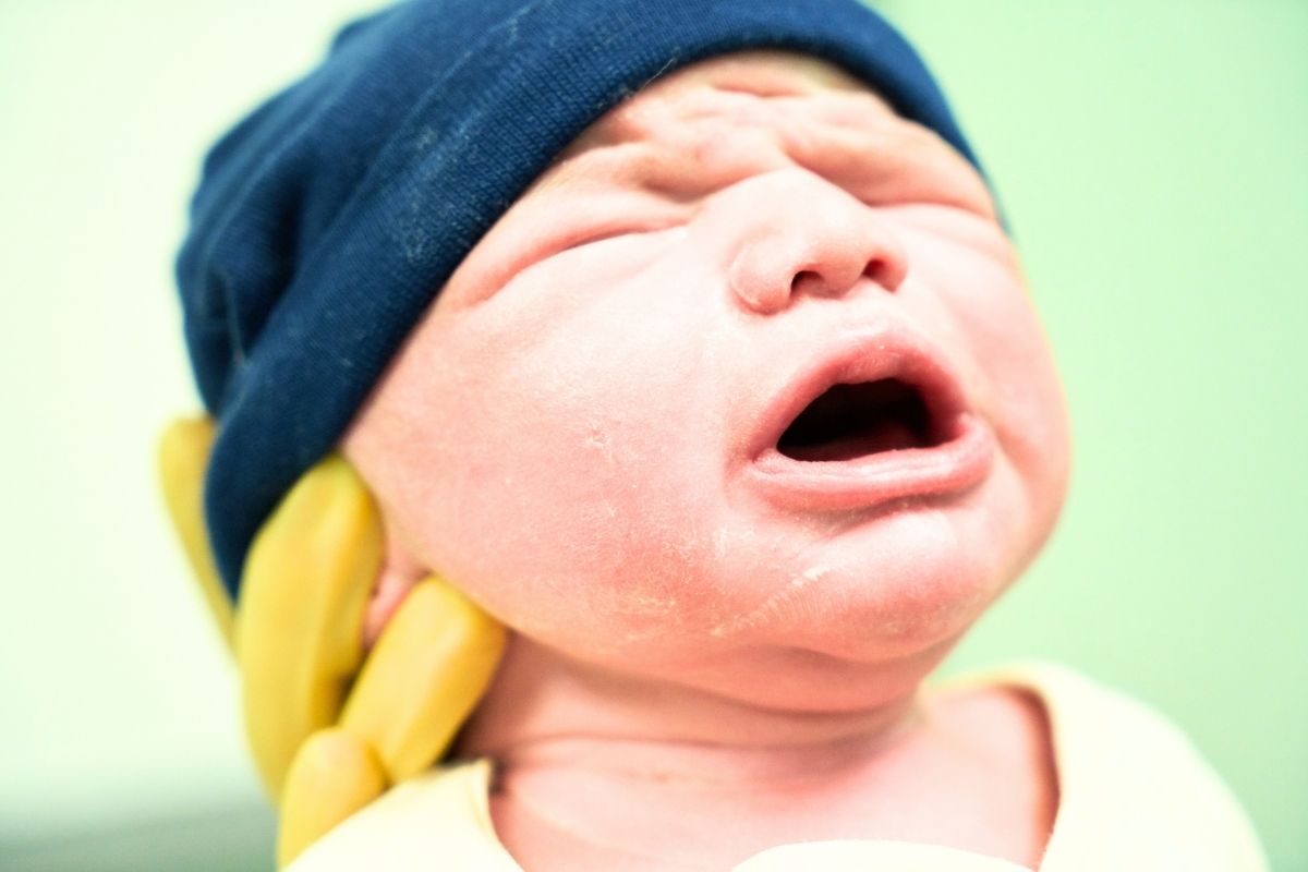 Newborn baby with a blue hat in hands with yellow medical gloves.