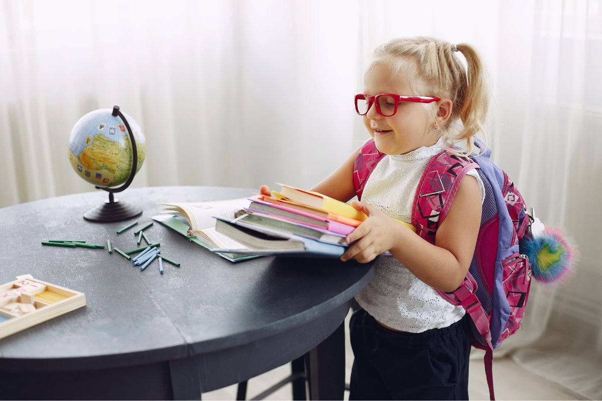 Young child wearing a backpack and gathering books while preparing for kindergarten.