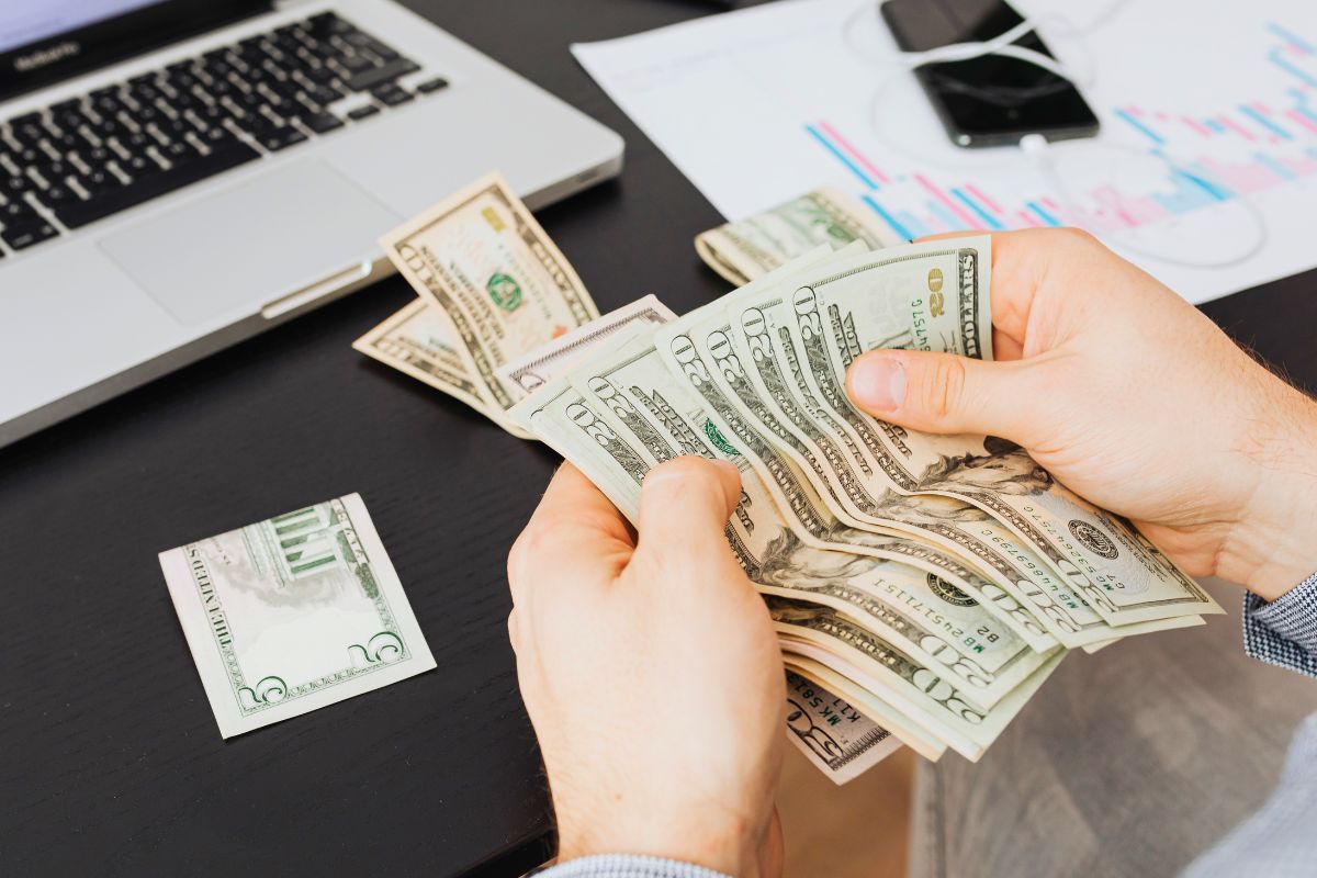 Counting cash and organizing finances while reviewing a family budget on a laptop.