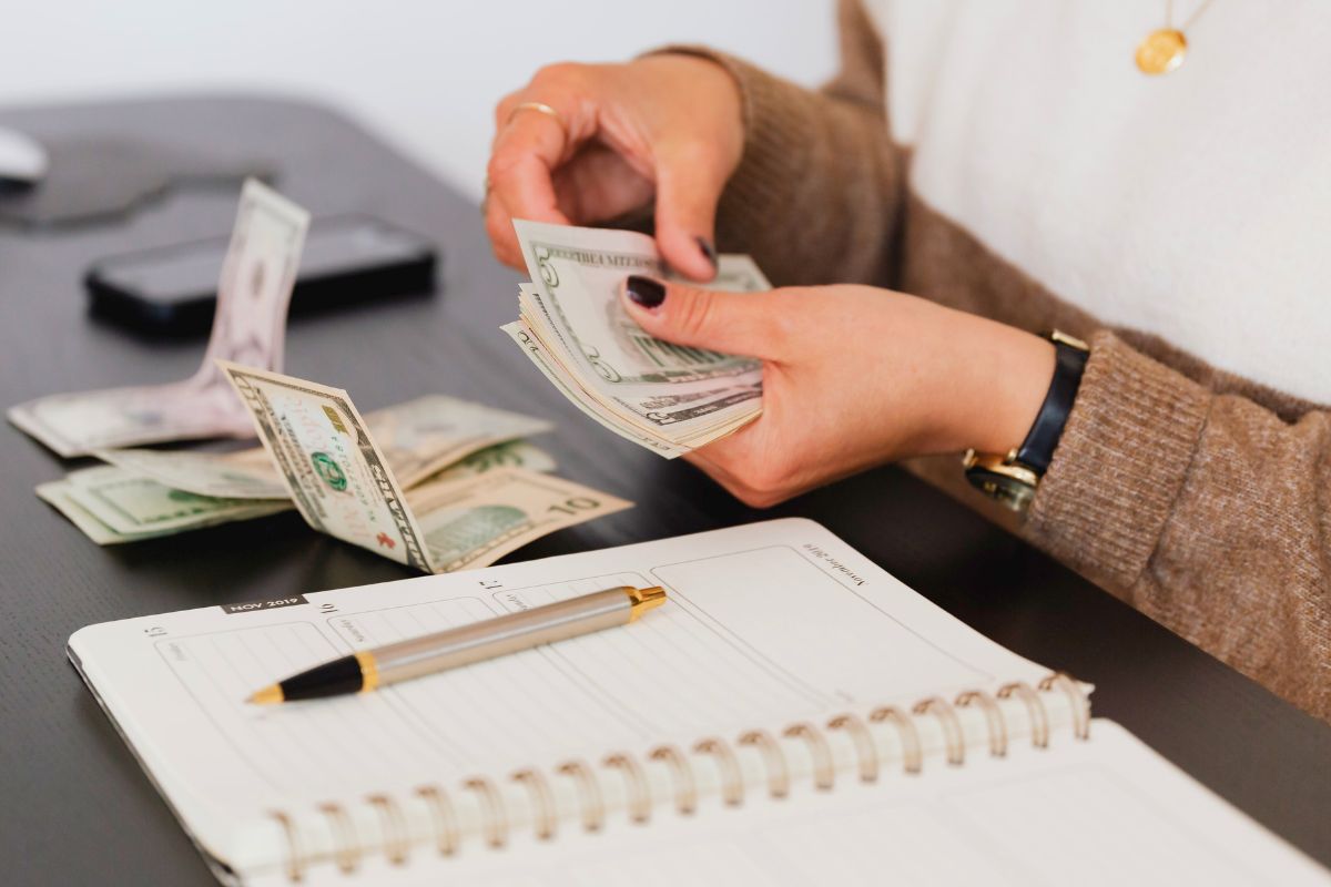 Woman counting money beside a planner while tracking spending and monthly expenses.