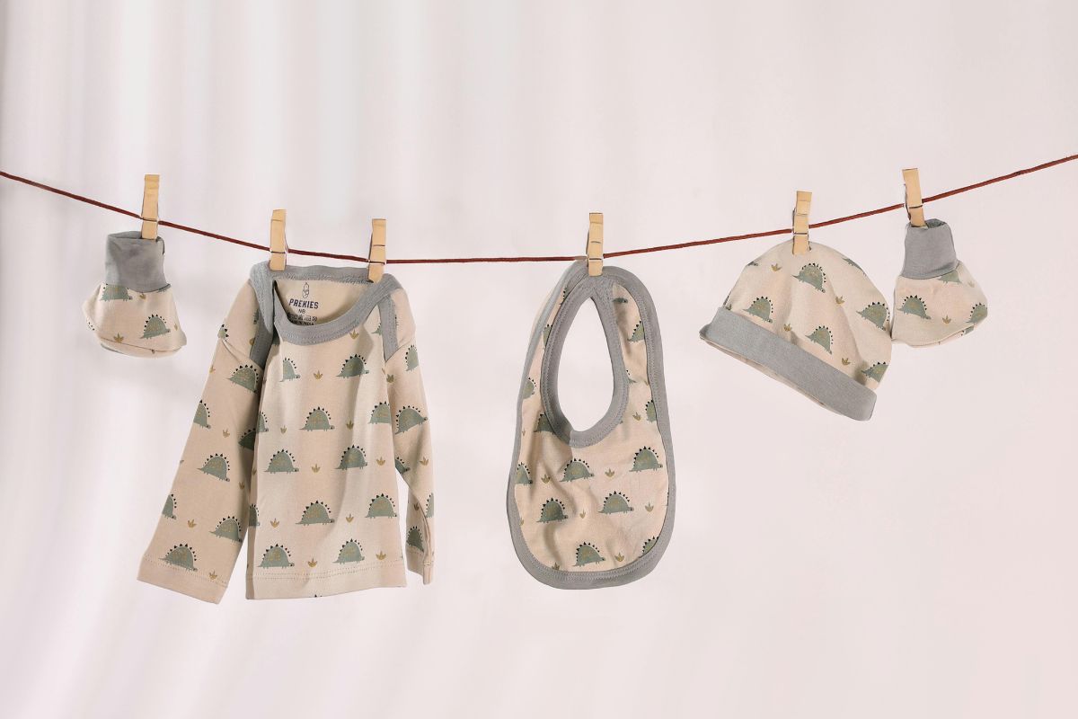 Baby clothes, bib, mittens, and hat hanging on a line as clothing essentials for a travel-friendly baby packing list.