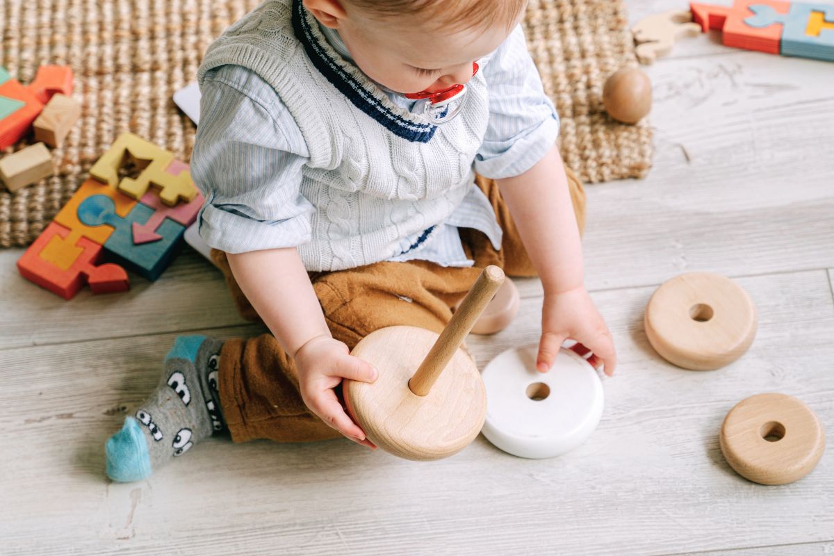 Baby playing with wooden toys on the floor, highlighting entertainment items for a travel-friendly baby packing list.