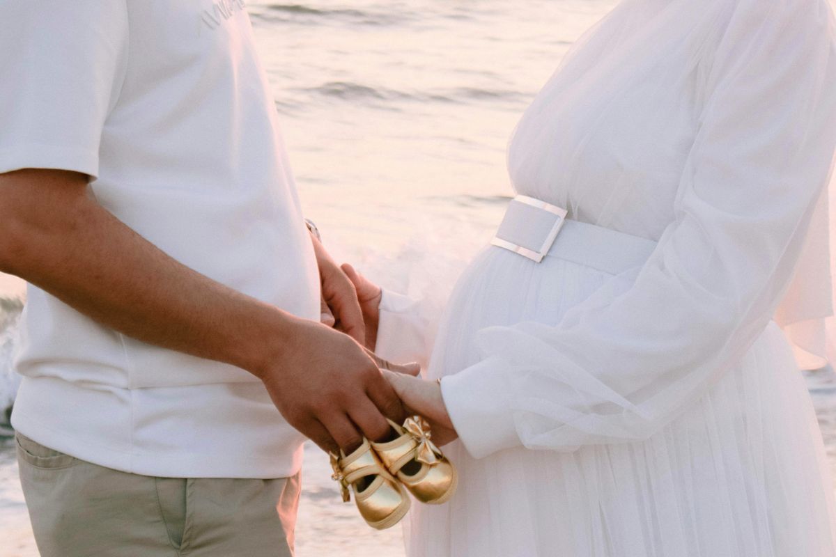 Expecting parents holding baby shoes during a peaceful beach babymoon before newborn life begins.