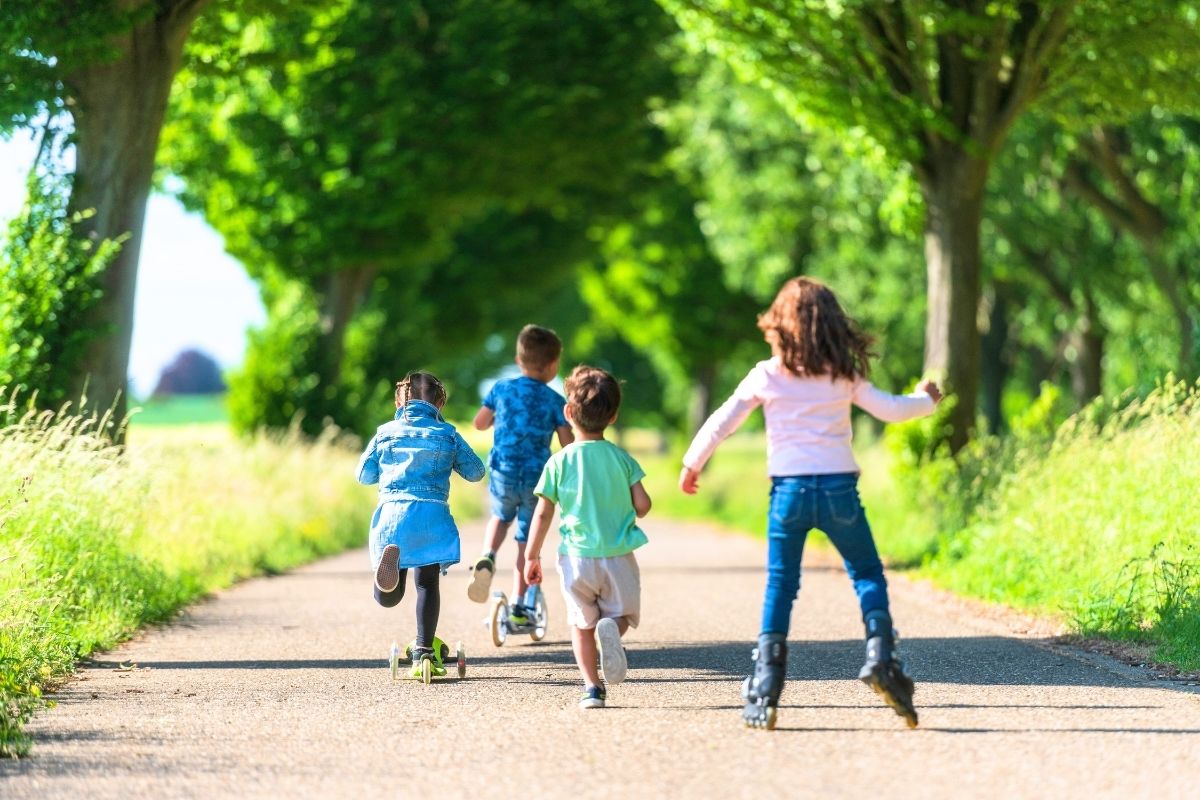 Children riding scooters together on a paved park path.