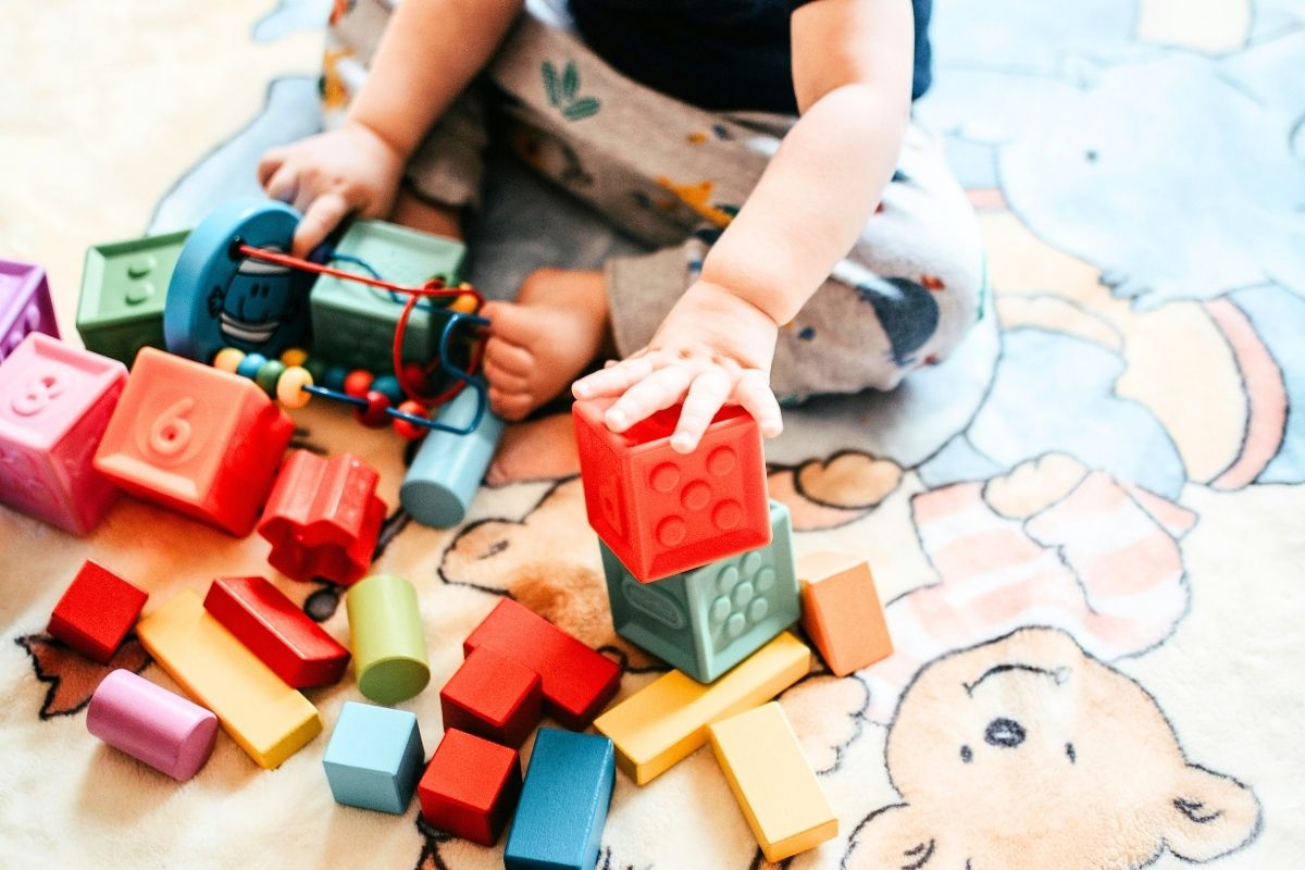 Baby sitting on a mat playing with colorful wooden blocks.