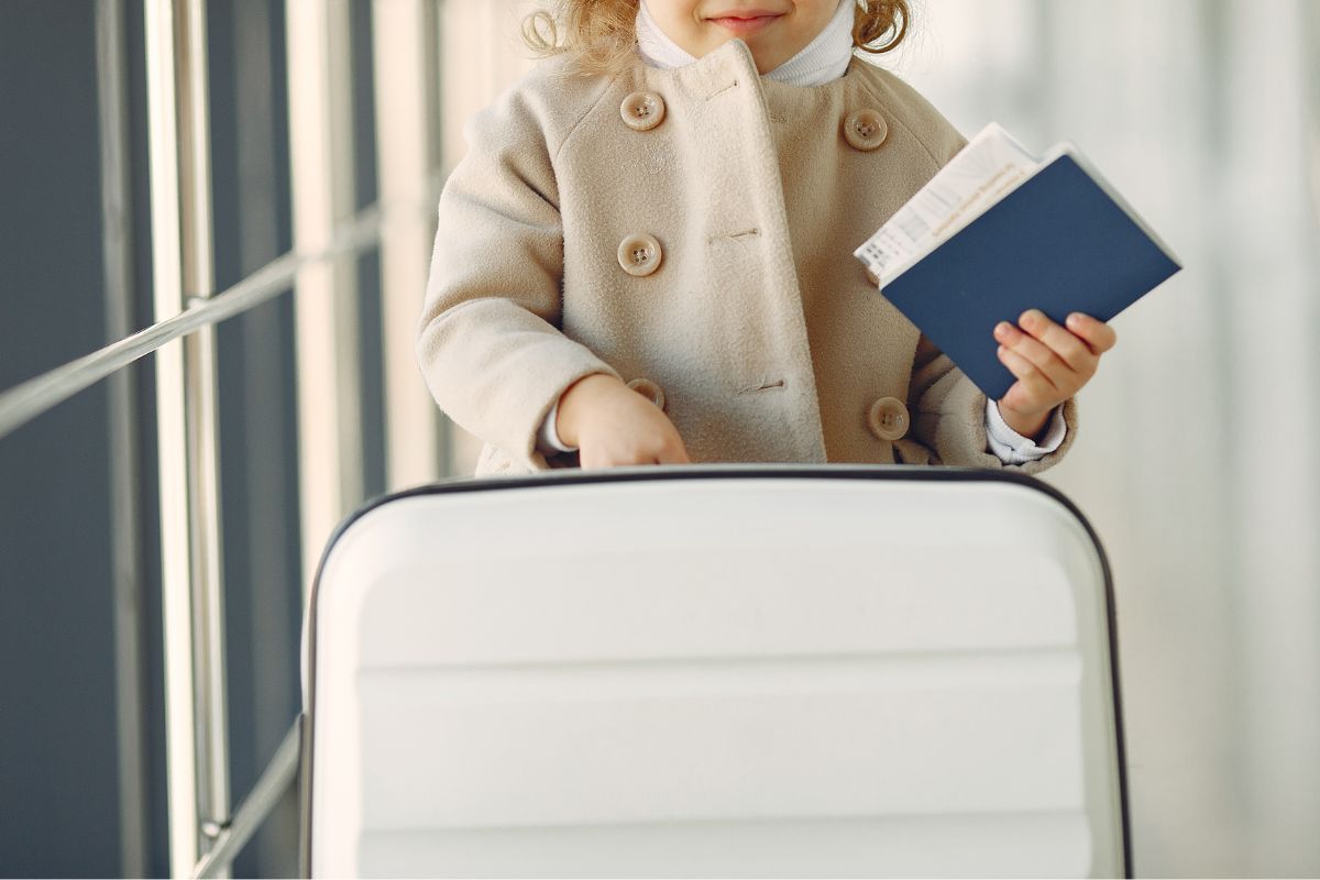 Child with passport and suitcase, kids travel carry on essentials.