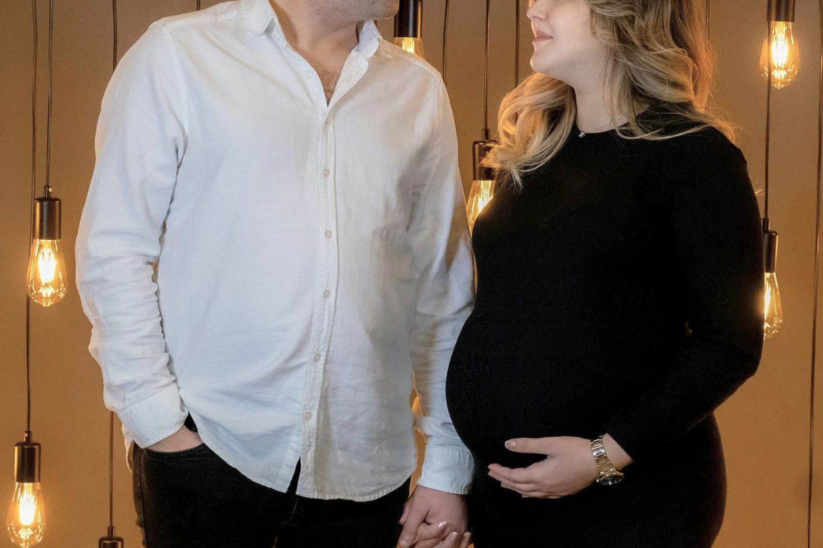 Expecting couple holding hands during a romantic indoor winter babymoon photoshoot.